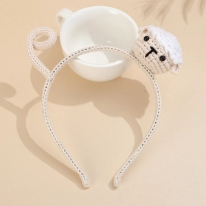 Detail of knitted headband featuring beige and white crochet sheep doll on neutral surface