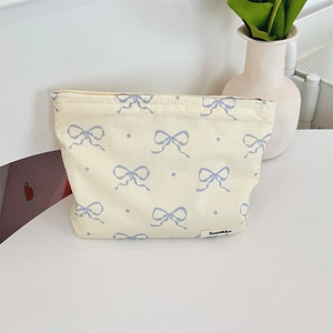 Detail of beige floral makeup bag with blue bow on a white desk with plants