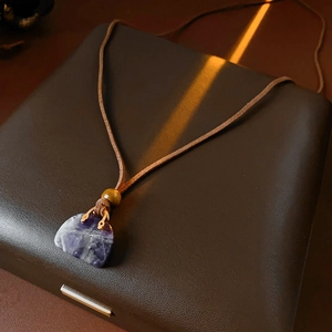 Macro detail of purple gemstone pendant with brown leather cord and wooden bead