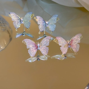 Détail de boucles d'oreilles papillon aux ailes translucides, strass et reflet miroir