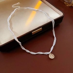 Detail of double-layer pearl necklace with a gold starburst pendant on a jewelry box