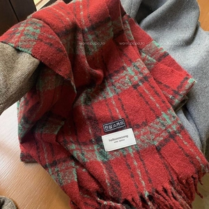 Detail view of red plaid winter scarf with thick wool texture and fringe on wooden surface