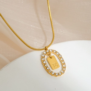 Detail of gold snake chain with oval pendant featuring pavé zircons and letter E