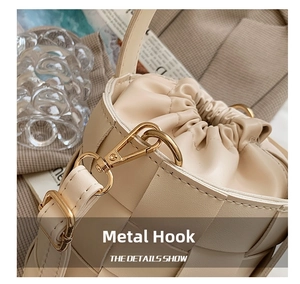 Detailed close-up of light gold metal hooks and woven leather drawstring on a beige bucket bag