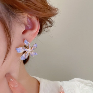 Gros plan de boucles d'oreilles fleurs en émail violet et bord doré portées par un modèle