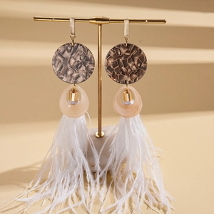 Detail of bohemian long feather earrings with resin marble disc on a gold stand