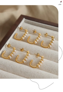Detailed close-up of golden U-shaped earrings with five white pearls in a wooden jewelry box