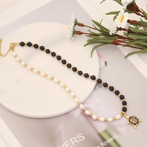 Black onyx and pearl necklace with colorful enamel turtle pendant on a white tray