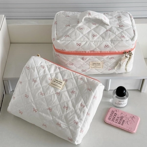 Détail de la trousse de maquillage matelassée avec nœuds roses et fermeture éclair orange