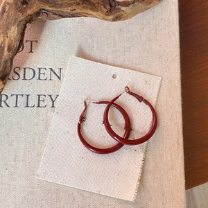 Detail of dark red geometric hoop earrings on linen card with retro book background