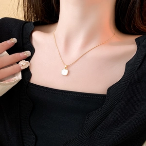 Détail d'un collier en titane doré avec un pendentif carré en nacre blanche élégant