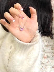 Close-up of pink heart pendant necklace with fine silver chain held by a person