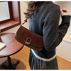 Detail of dark brown suede and leather shoulder bag with metallic buckle on model