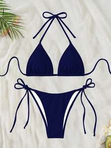 Flat lay of navy blue ribbed string bikini with sunglasses and tropical leaves on white fabric