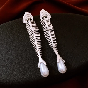 Detailed view of silver fishbone earrings featuring a teardrop pearl on a black surface