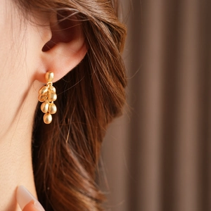 Close-up of model wearing matte golden beaded drop earrings with a minimalist aesthetic