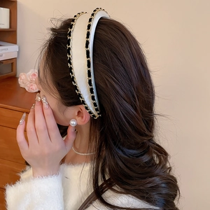 Detail of white padded fabric headband featuring classic black and gold woven chain trim