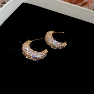 Macro shot of gold crescent moon earrings with shimmering zircon pavé on black velvet