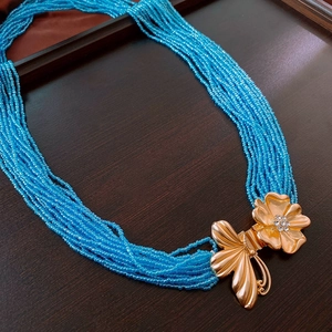 Détail de la chaîne perlée bleue avec boucle papillon et fleur dorée sertie