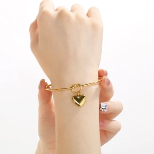 Bracelet jonc doré en forme de C avec pendentif coeur poli porté par un mannequin