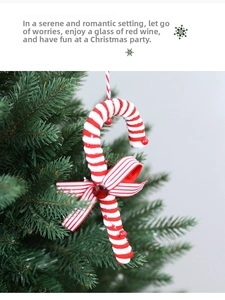 Detail of red and white striped candy cane ornament with bow on green Christmas tree