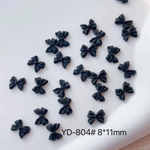 Macro view of matte black 8x11mm resin bow nail charms for professional manicure art