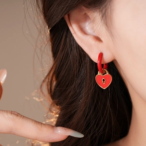 Close-up of red heart lock earrings with golden keyhole detail worn by a model
