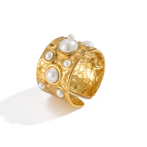 Bague ouverte large en métal martelé doré ornée de perles sur fond blanc