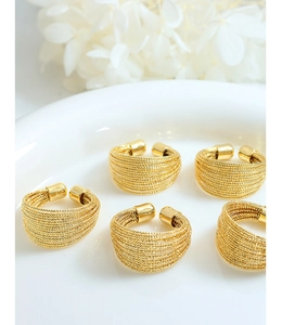 Close-up of five adjustable gold rings with twisted wire texture on a white plate