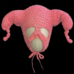 Detail of pink hand-crocheted devil horn hat with ear flaps and knit texture on model