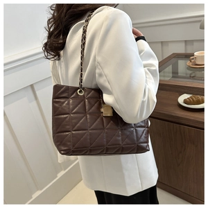 Détail du sac cabas matelassé marron foncé avec chaîne dorée sur un blazer blanc