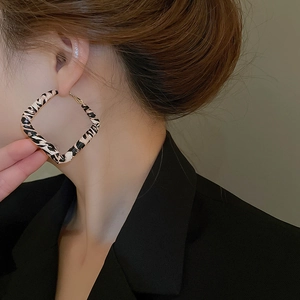 Close-up of leopard print square hoop earring worn on ear with golden metal accents