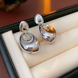 Detailed view of polished silver drop earrings on a beige velvet jewelry box cushion