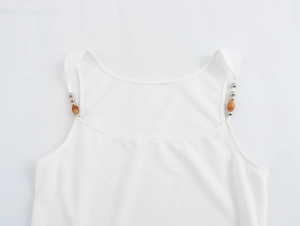 Close-up of white camisole top featuring decorative metal and wood beads on shoulder straps