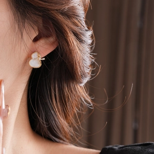 Detail of model wearing gold-plated gourd stud earrings with white shell and cross charms