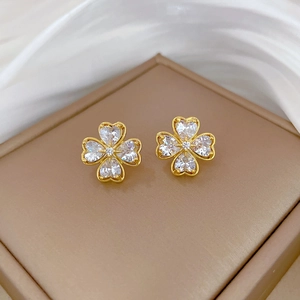 Detail of four-leaf clover stud earrings with heart-shaped crystals on a silk background