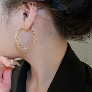 Detailed close-up of a model wearing double-layered golden twisted geometric hoop earrings