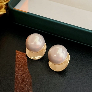 Detailed close-up of large round pearl earrings with irregular gold metal base