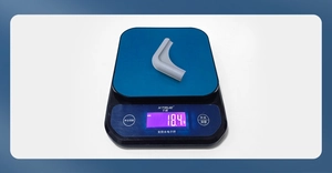 Detailed view of grey L-shaped silicone corner guard weighing 18.4g on a digital scale