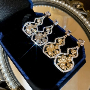 Detail of hollow gourd earrings in gold and silver finish with sparkling zircon stones
