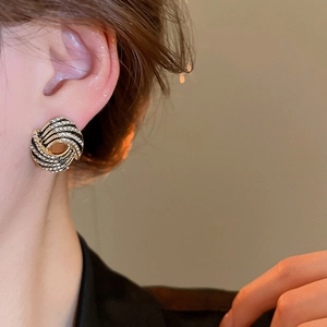 Macro shot of gold spiral rhinestone earrings featuring black enamel details on model