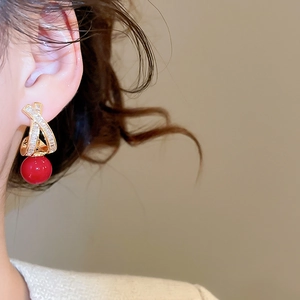 Detailed close-up of a gold-plated crossover stud earring with red pearl and pavé crystals