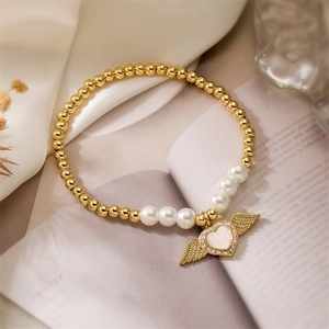 Detail of gold beaded bracelet featuring a shell heart wing pendant and white pearls