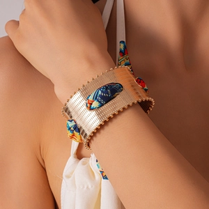 Detail of gold metal open cuff bracelet woven with colorful silk scarf on model's wrist
