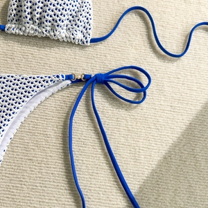 Detail of white crochet knit bikini featuring blue straps with gold rings and pearls