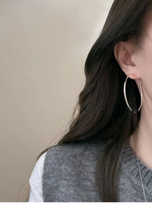 Side view of a large silver C-shaped hoop earring worn on a model's ear