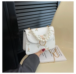 Detail of floral embroidery on white square bag with pearl handle and gold chain