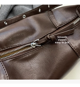 Detailed macro view showing a smooth silver metal zipper on dark brown leather tote bag