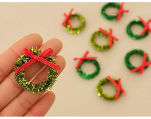 Close-up of mini green Christmas wreaths with red bows held in hand for scale