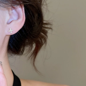 Macro shot of gold cross stud earrings featuring a textured frosted finish on model's ear